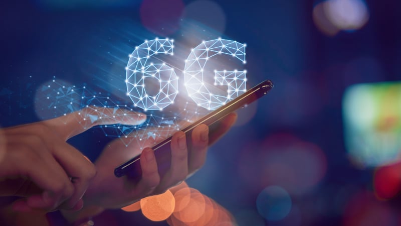 6G: Zwei Hände halten ein Smartphone. Darüber ein 6G-Symbol.